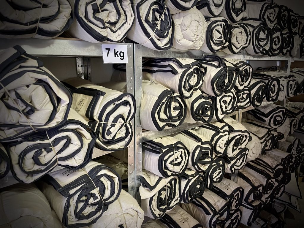 Flere sammenrullede 7 kg tyngdedyner ligger organiseret på metalhylder hos RestfulBlanket. Flere sammenrullede 7 kg tyngdedyner ligger organiseret på metalhylder hos RestfulBlanket.