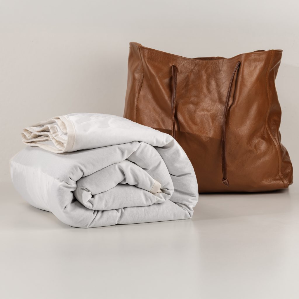 Kugledyne vs tyngdedyne: Naturlig tyngdedyne fra RestfulBlanket i lys sandfarve med tilhørende taske, vist som roligt alternativ til klassisk kugledyne.
