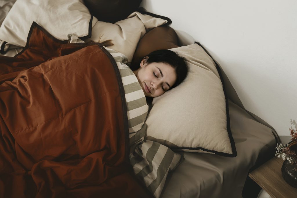 Voksen kvinde sover roligt under brun RestfulBlanket tyngdedyne i naturlig bomuld.