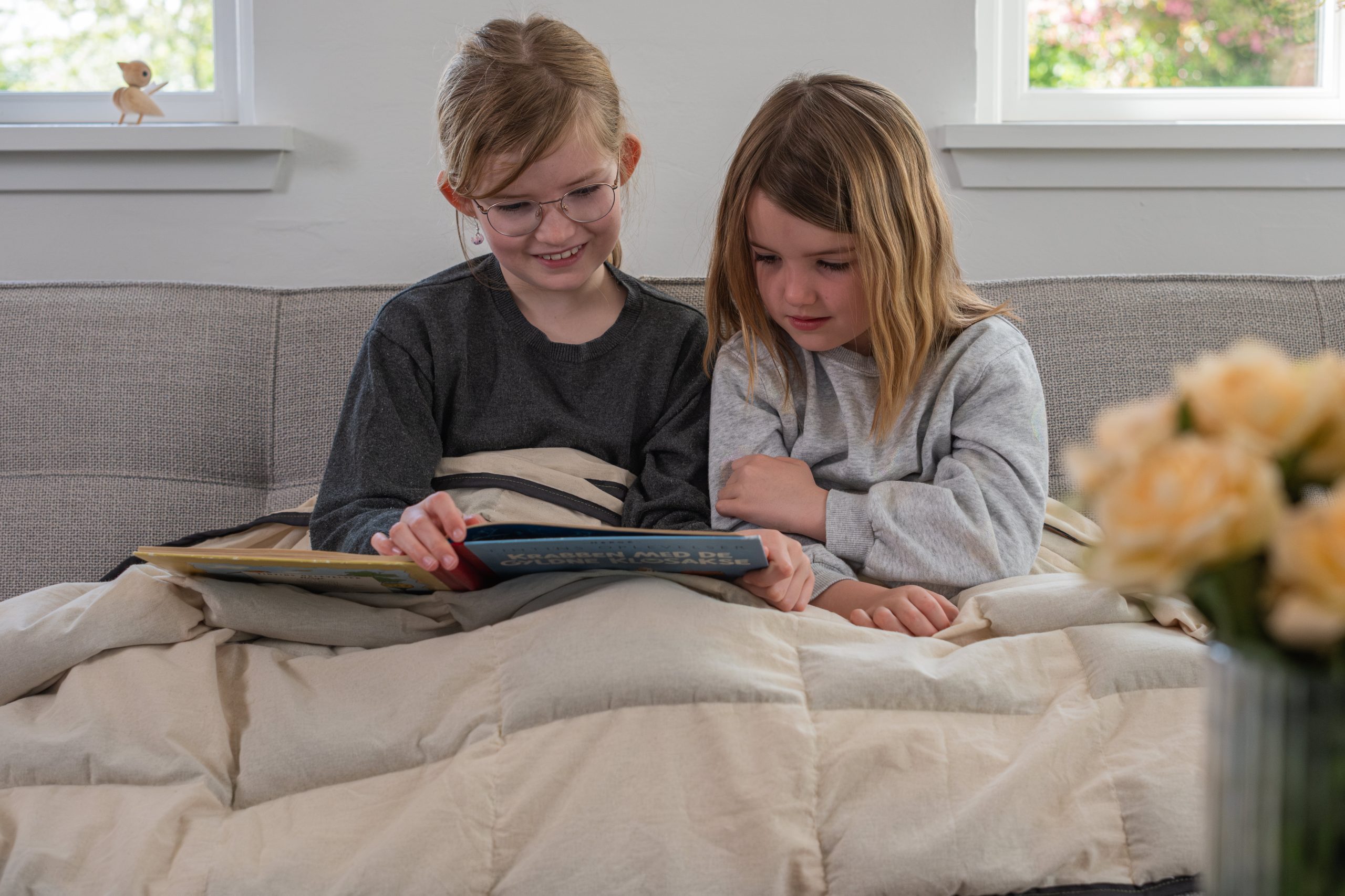 To børn sidder og læser under en naturlig tyngdedyne fra RestfulBlanket som eksempel på tyngdedyne til børn