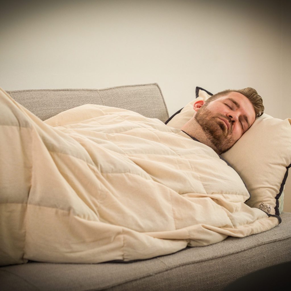 Voksen mand sover roligt paa sofaen under en naturlig tyngdedyne fra RestfulBlanket